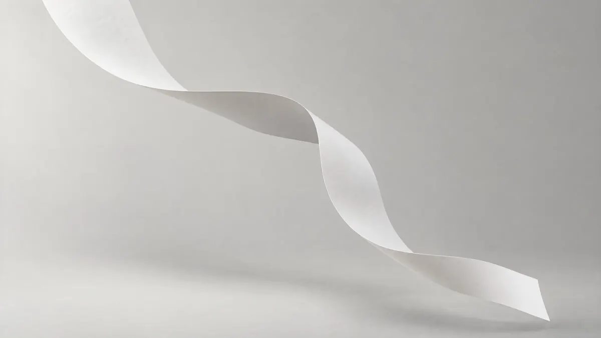 A white paper ribbon flows through the air in a soft S against a pale grey backdrop, showing a slightly deeper tone where it turns.
